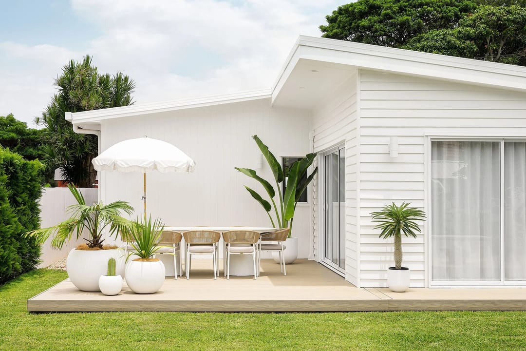 Pale Ekodeck Designer Series Backbeach deck with outdoor dining and a white umbrella beside a white weatherboard home