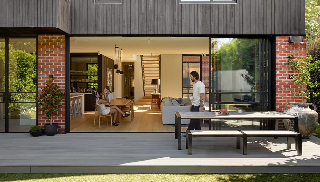 Light grey Ekodeck Summit Series Stirling deck with outdoor dining table behind a brick and timber home