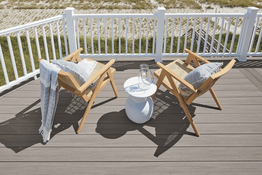 Grey Coastline deck with two timber armchairs and a white side table behind a white railing, dune grass beyond