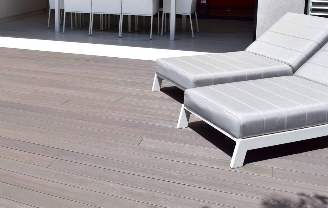 Graphite deck with two white sun loungers in front of an outdoor dining area