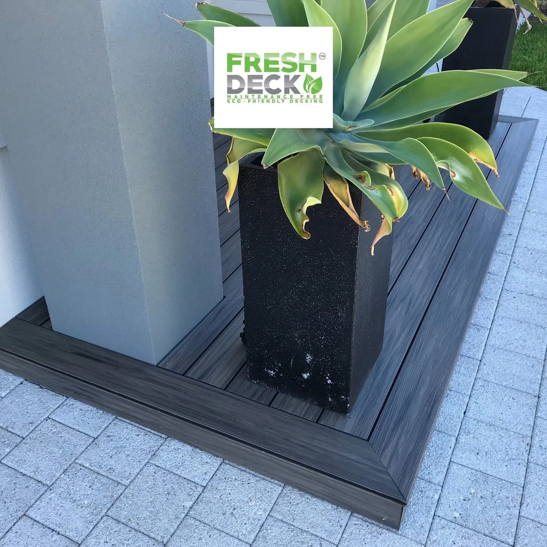 Dark grey FreshDeck deck with a matching fascia edge around a tall black planter on pale pavers