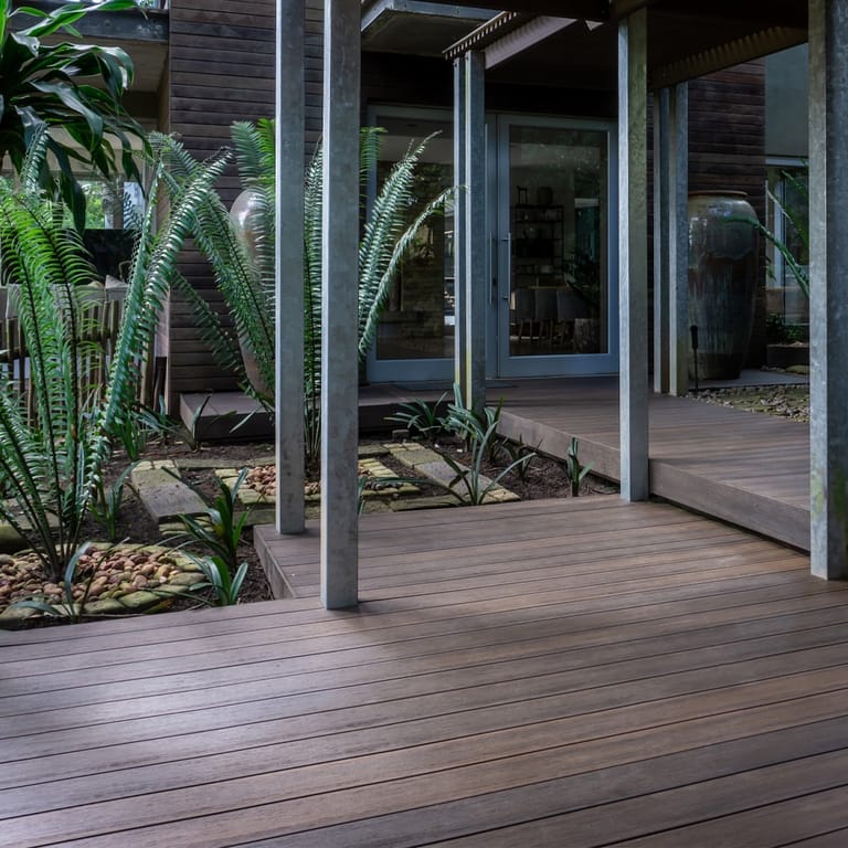 Eva-Last Infinity Tiger Cove deck beneath a modern house with steel posts, glass doors and a tropical garden