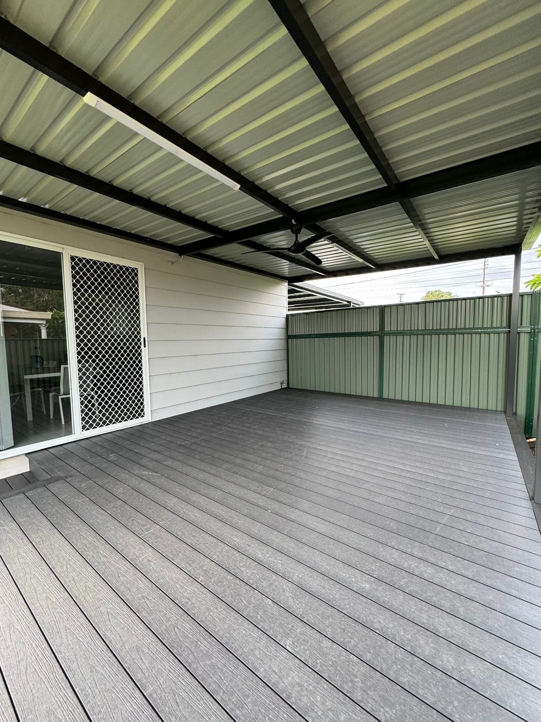 Grey Acetech deck under a new skillion patio roof outside sliding doors, enclosed by a green steel fence
