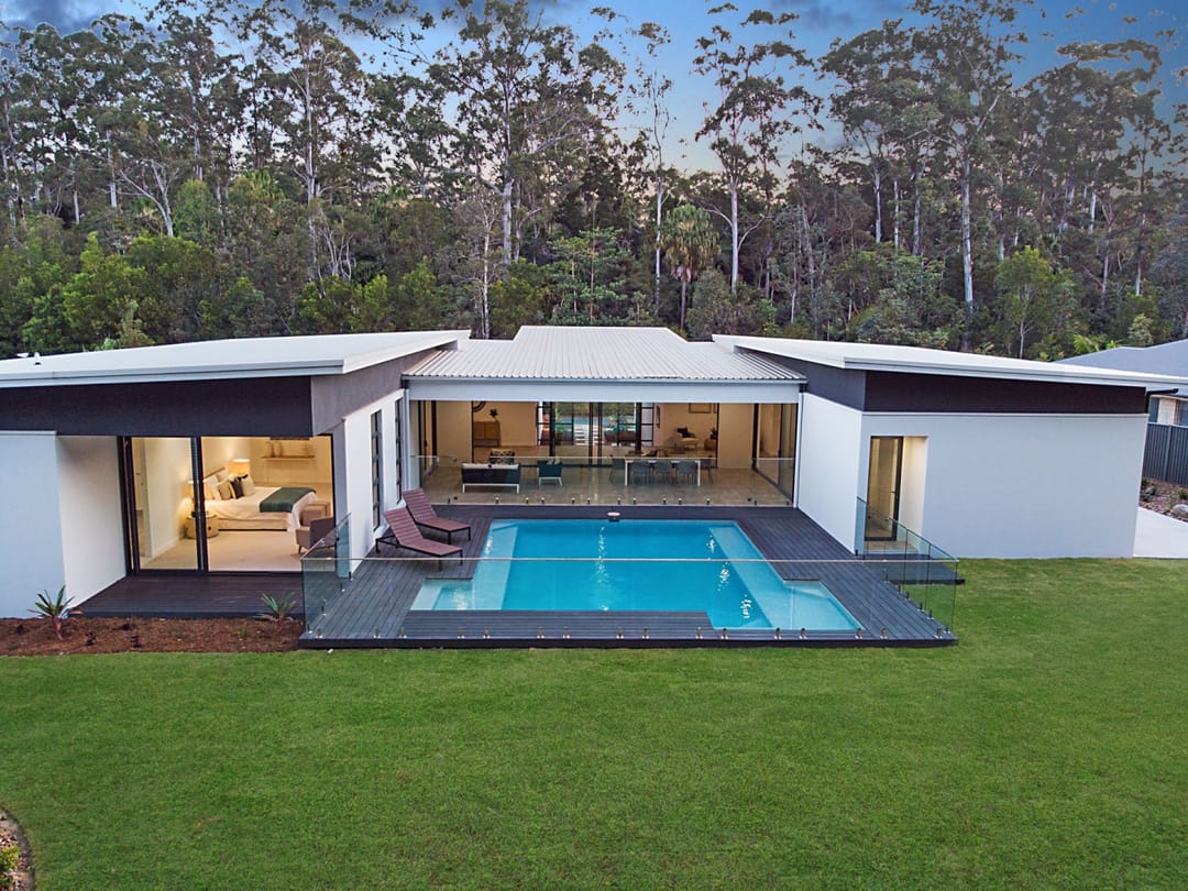 Dark grey composite deck around a swimming pool at a modern single-storey home backing onto bushland