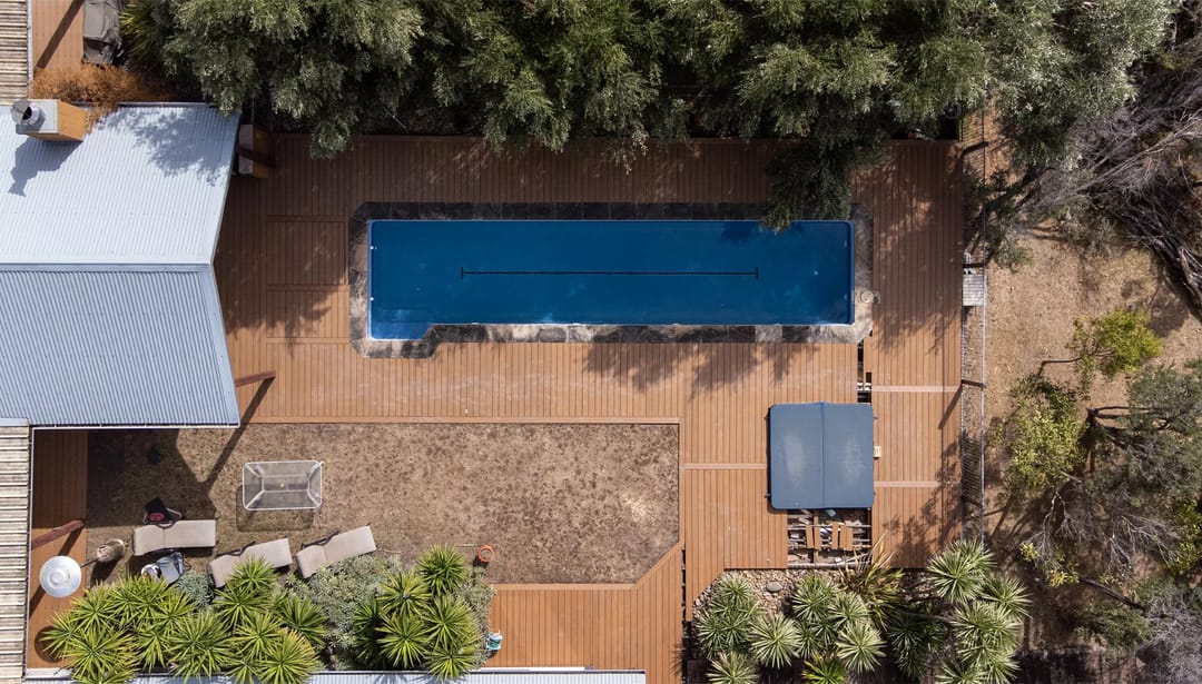 Aerial view of a brown Ekodeck Designer Series Leatherwood deck surrounding a rectangular pool and garden beds