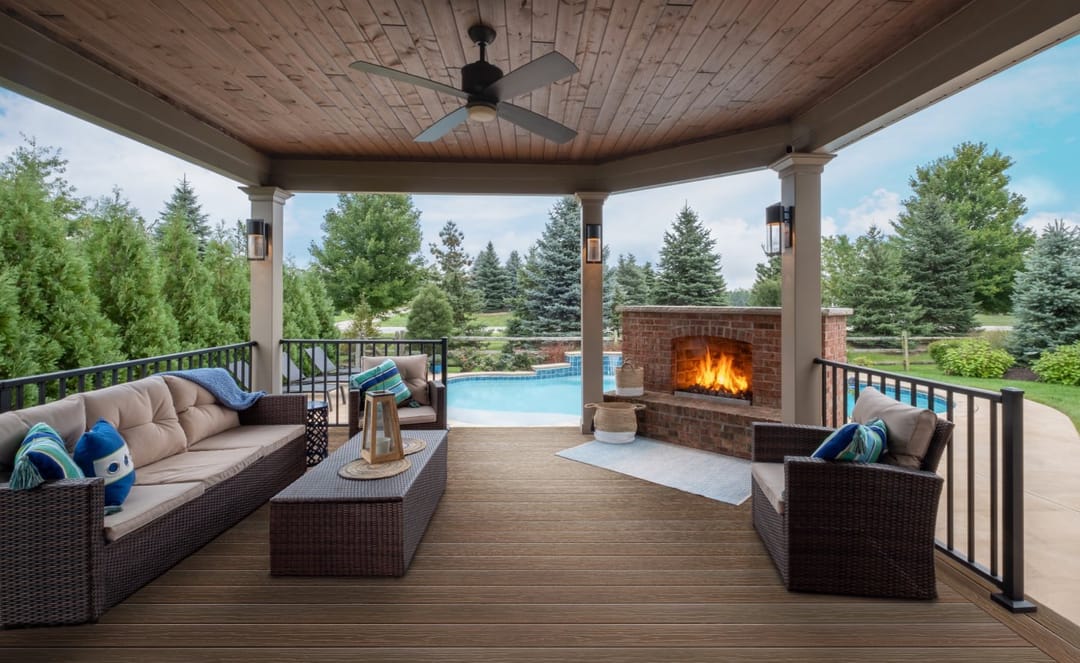 Cold Brew deck in a covered pavilion with wicker sofas, a stone fireplace and ceiling fan, a pool beyond