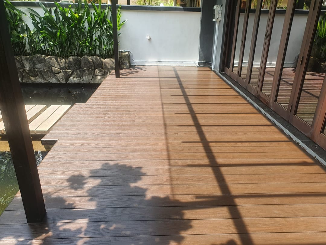 Covered Biowood deck in warm brown boards outside full-height sliding doors, with tropical planting and timber posts