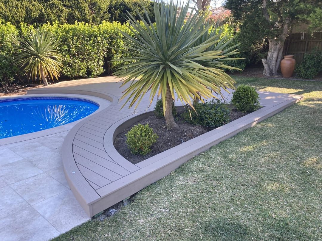 Curved light greige Rope Swing deck edging a kidney-shaped pool and a garden bed of spiky yuccas