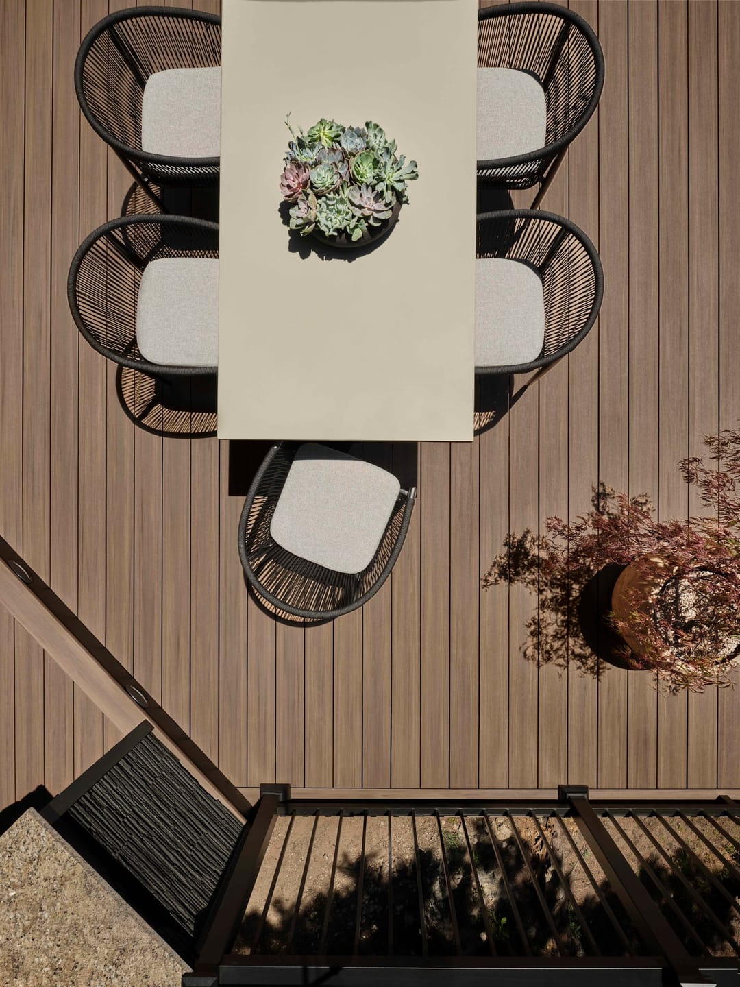Overhead view of an outdoor dining table with black chairs on English Walnut decking beside a black stair rail