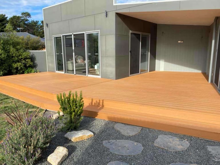 Light brown ModWood Natural Grain Sahara deck outside a modern rendered home, with stepping stones and a gravel garden