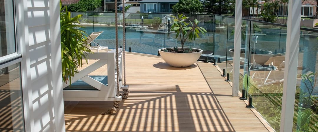 Light timber-look Origin composite deck on a canal-front balcony with glass balustrade, hanging day bed and planter