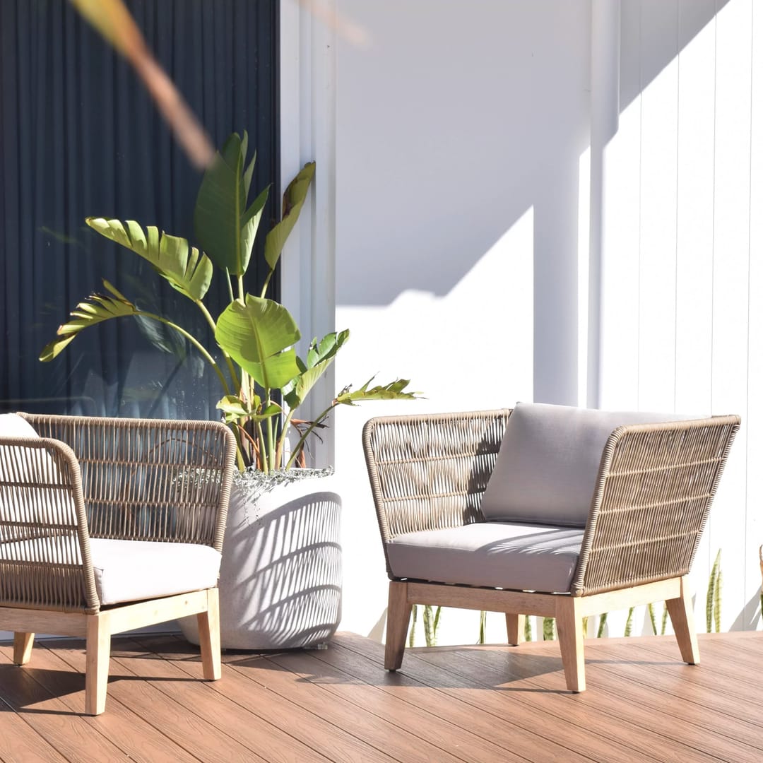 Ekodeck Flame Fighter Honey Oak deck with two woven outdoor armchairs and a potted plant against a white wall