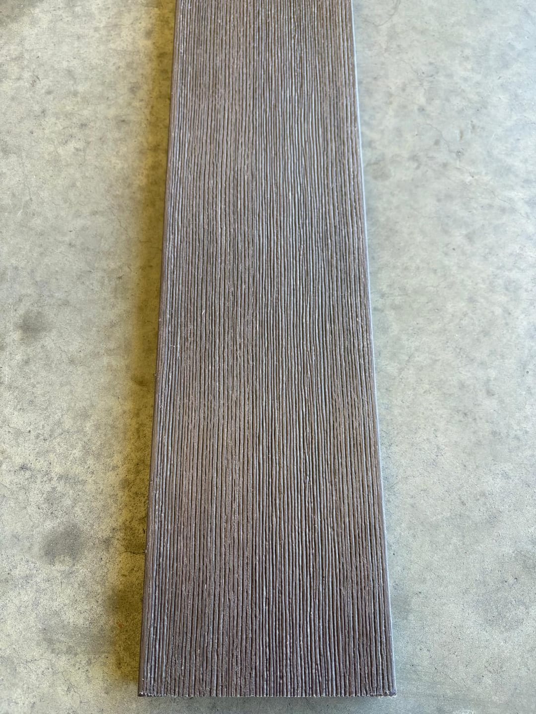Modelo Prime Ipe solid composite deck board lying on a concrete floor, showing its dark brown brushed wood-grain face