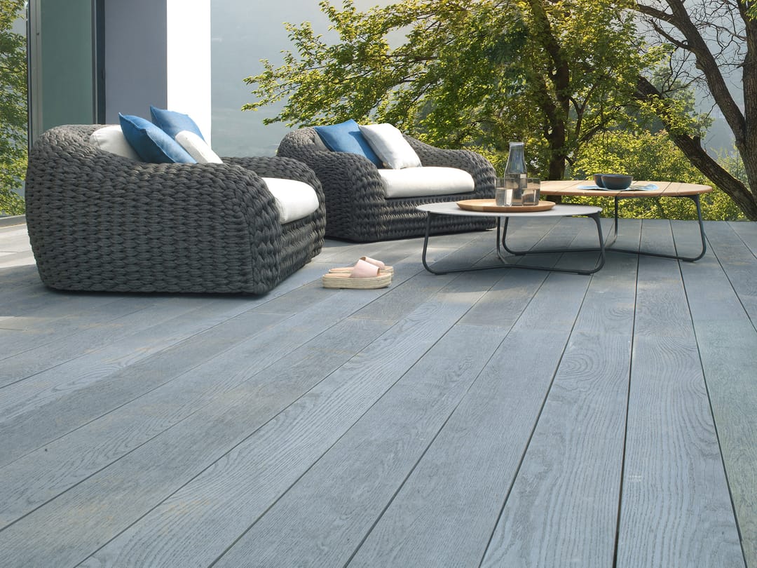 Blue-grey Brushed Basalt deck with two woven armchairs and a low table under a tree beside a modern house