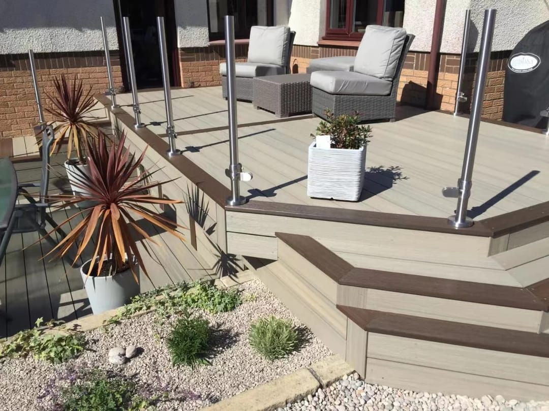 Two-tone PureSolid composite deck with steps, glass balustrade, pot plants and outdoor lounge chairs outside a brick house