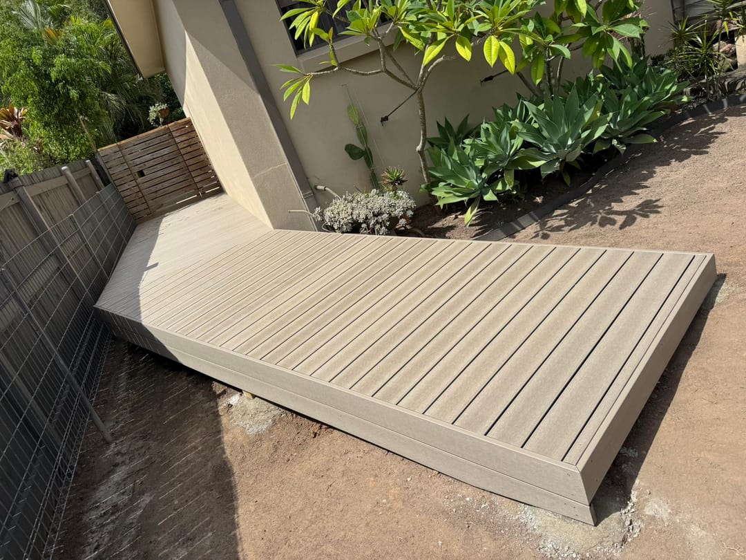 Small pale greige composite deck platform built into a garden corner beside a rendered planter wall