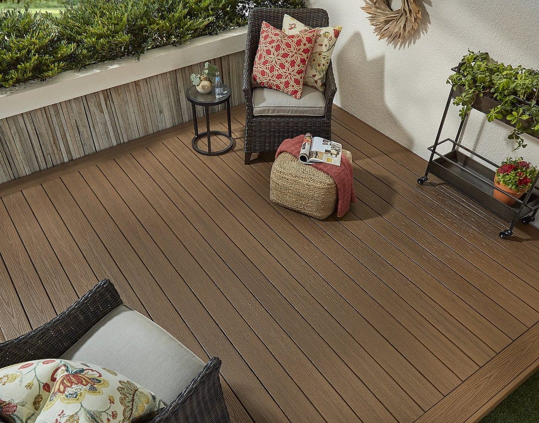 Brown Stringybark deck styled with a wicker armchair, floral cushions, a pouf and plant stand against a white wall