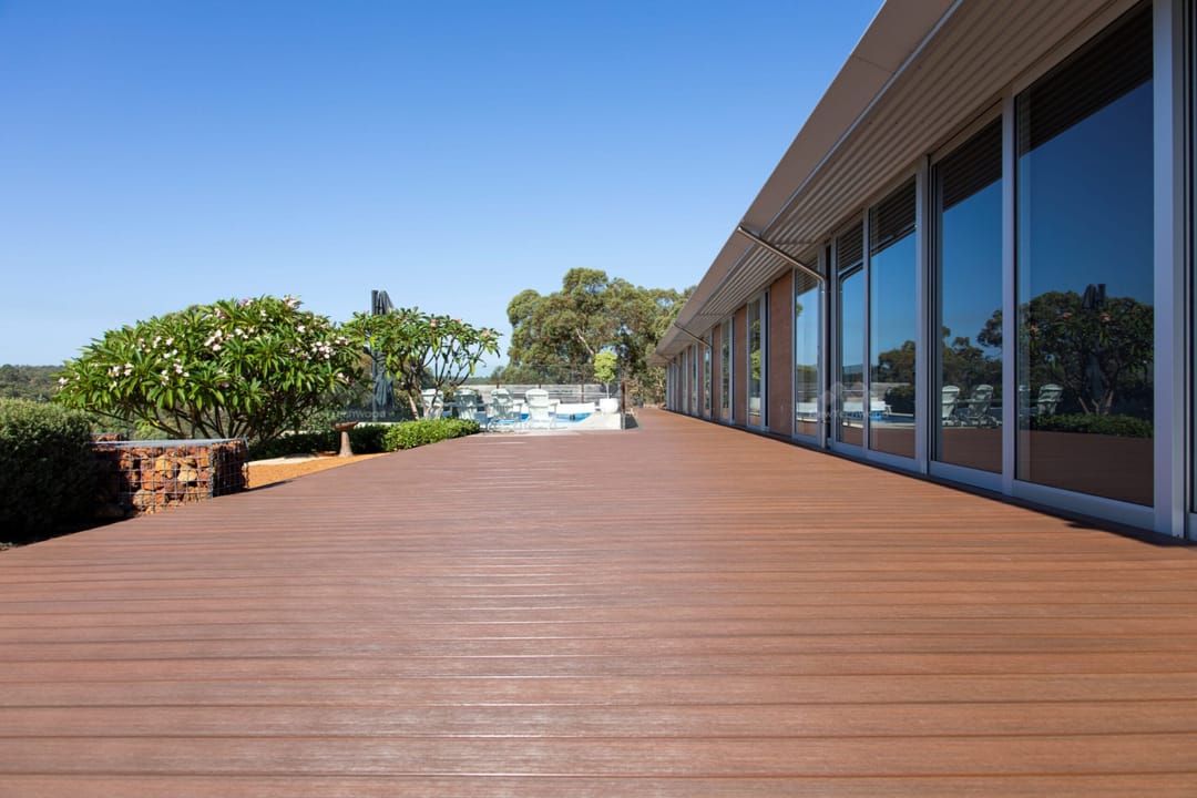 Long NewTechWood Avenue Walnut deck running along a glass-fronted home, garden and pool fence beyond, Perth