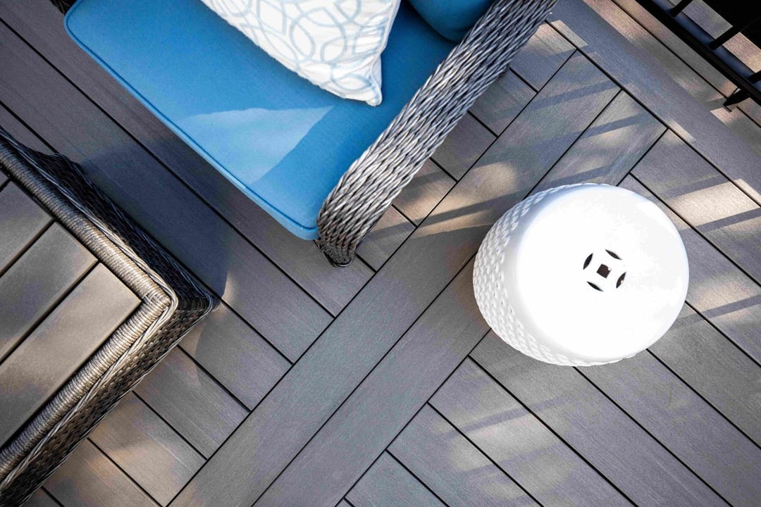 Overhead view of dark Black Oak decking with a wicker chair, blue cushion and white ceramic garden stool