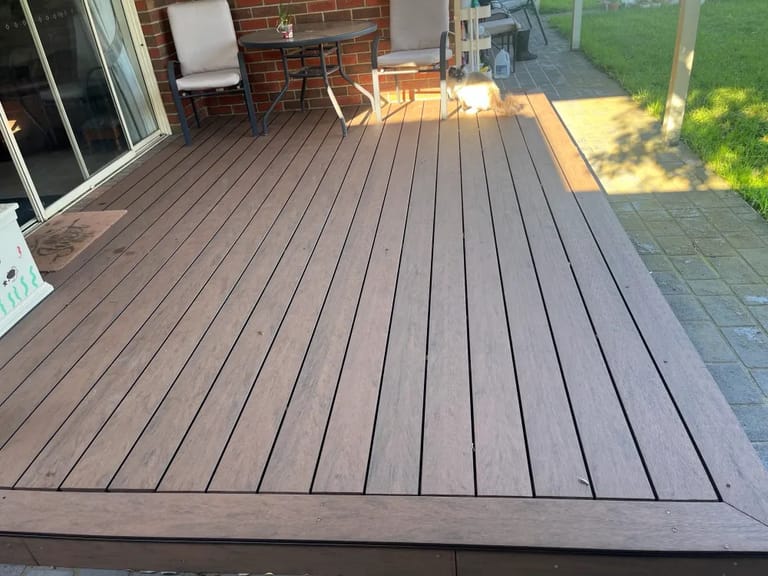 Ground-level patio deck in CleverDeck Eco-Pro Black Bean beside a brick house and lawn, with a picture-frame border