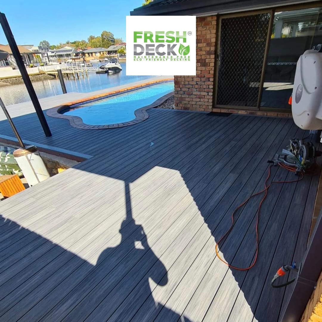 Freshly laid grey FreshDeck composite deck beside a pool on a canal-front property, power tools still on the boards